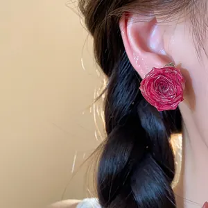 Detailed close-up showing a realistic red rose stud earring worn on a model's ear.