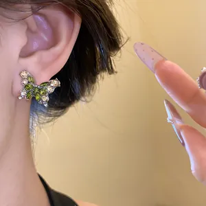 Gros plan de boucles d'oreilles papillon en argent avec zircons verts portées à l'oreille