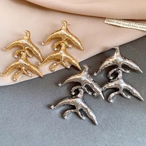 Close-up of gold and silver hammered metal swallow earrings with pearl accents