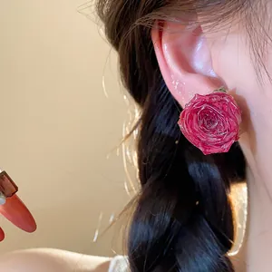 Close-up view of a resin-preserved red rose stud earring worn on ear.