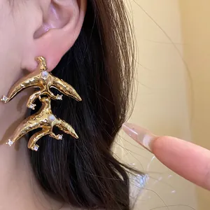 Detailed view of vintage gold swallow drop earrings with pearls and rhinestones on model