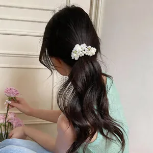 Elegant pearl and white fabric flower hair tie securing a ponytail on long dark wavy hair