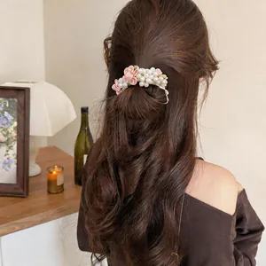 Detailed view of sweet pearl and pink fabric flower hair clip on wavy brown hair
