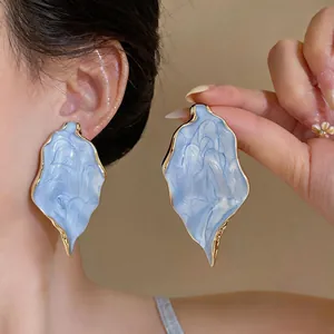 Close-up of oversized light blue textured drop earrings with gold trim on model
