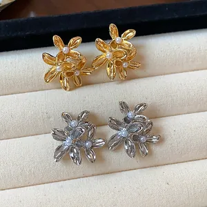 Detailed close-up of gold and silver floral stud earrings with pearls in a box