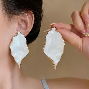 Detail view of oversized white pearlescent leaf earrings with gold-tone borders.