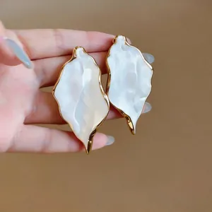 Macro view of oversized textured leaf earrings with gold trim held by model's hand