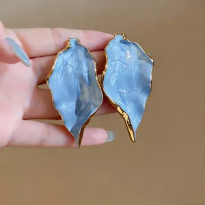 Detailed macro view of oversized blue leaf earrings with gold-toned textured borders.
