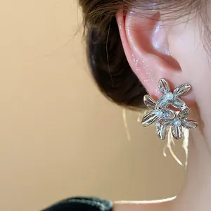 Close-up detail of silver floral stud earrings with pearl centers on ear.