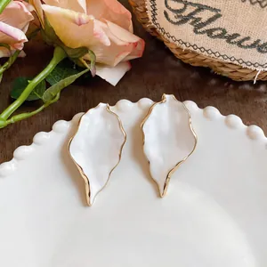 Close-up of elegant white leaf earrings with gold-toned metal edges on a white ceramic plate.