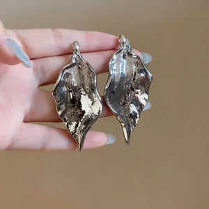 Close-up of oversized metallic earrings with wrinkled texture and silver finish