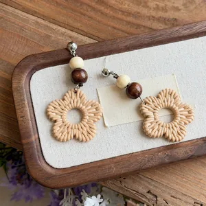 Handmade bohemian rattan woven floral earrings with wooden beads on a rustic wooden tray