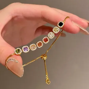 Close-up of gold adjustable bracelet with vibrant multi-colored square gemstones.