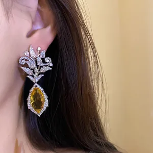 Detailaufnahme der Zirkon-Blumen-Ohrhänger mit einem gelben Marquise-Stein am Ohr eines Modells.
