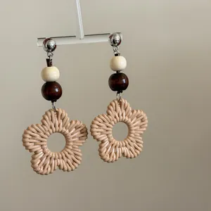 Close-up of bohemian woven rattan flower earrings with wooden beads on display stand.
