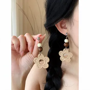 Close-up detail of bohemian rattan flower woven earrings featuring dark wooden beads