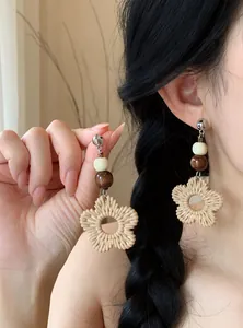 Detailed close-up view of bohemian style rattan flower and wooden bead earrings on a model.