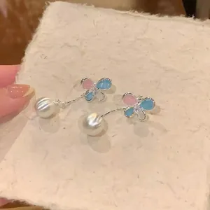 Close-up of elegant butterfly earrings with pink and blue wings and pearl drops.