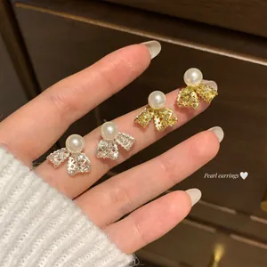 Close-up of elegant bow-shaped pearl stud earrings in gold and silver finish