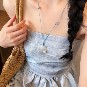 Detailed shot of a summer blue rope necklace with pearl and shell pendant