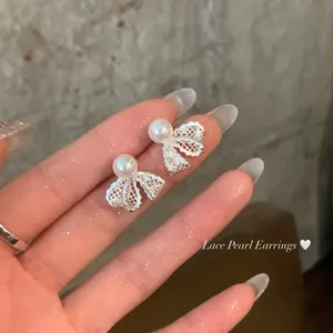 Macro view showing the intricate lace-textured bow earrings with elegant white pearls