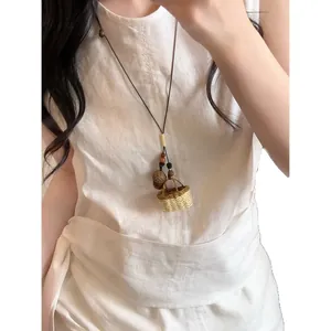 Collier d'été bohème fait main avec pendentif panier tissé et pomme de pin sur lin blanc