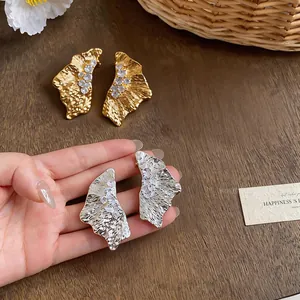 Detailed view of irregular pleated earrings with zircon insets on wooden surface