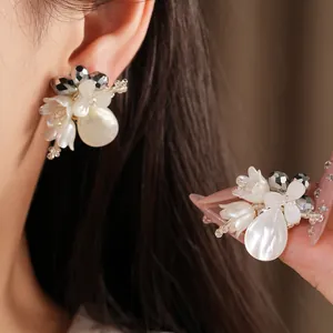 Macro detail of elegant white floral earrings with shell petals and teardrop pearls