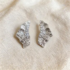 Detailed macro view of silver-tone textured wing earrings set with sparkling zircons.