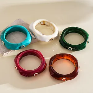 Group of colorful resin geometric bangles with rhinestone inlays in a still life setting.
