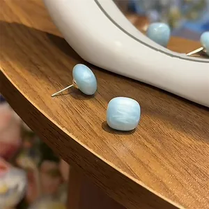 Detailed macro view of elegant blue enamel square stud earrings on a natural wood surface