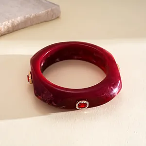 Macro detail of wine red resin bangle with square geometry and crystal embellishments.