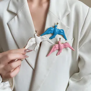 Close-up of three swallow-shaped enamel brooches in white blue and pink on a blazer
