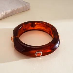 Close-up of a tortoiseshell resin bangle with orange gemstone and rhinestone inlay