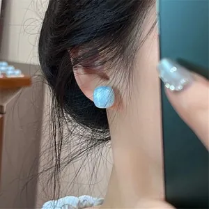 Close-up view of a minimalist light blue square drip oil stud earring on a model's ear