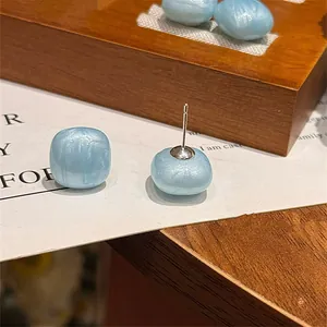 Close-up of light blue pearlescent square ear studs with silver needle backing