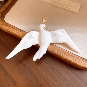 Close-up of a vintage-style white enamel bird brooch with elegant gold accents.