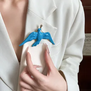 Elegant blue enamel swallow bird brooch with gold branch pinned on a white blazer