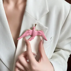 Close-up of elegant pink enamel swallow brooch with gold star detail on white blazer.