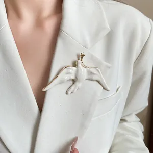 Close-up detail of a white enamel bird brooch with golden edges on a elegant white blazer.