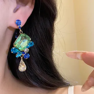 Close-up of vintage gold-plated drop earrings with green and blue square crystals