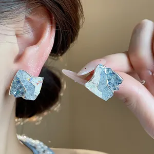 Dettaglio ravvicinato di orecchini a lobo geometrici in vetro celeste con perni in argento