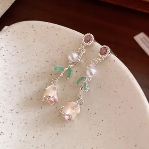 Close-up detail of delicate rose earrings with pink zircon, pearl and green enamel leaves.