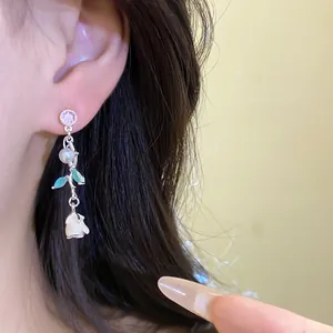 Close-up of floral drop earrings with white rose bud, pearl, and green enamel leaves