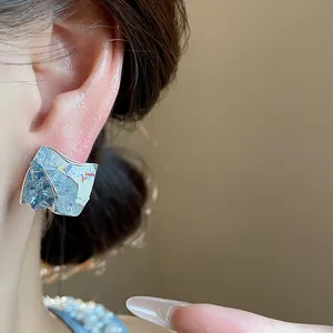 Dettaglio di orecchini a perno geometrici in vetro con riflessi blu cangianti