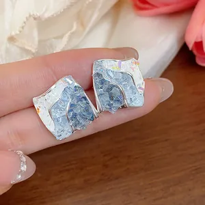 Dettaglio di orecchini a lobo in vetro a rombo con texture cristallina blu e argento