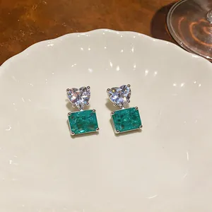 Close-up of heart-shaped zircon and green square gemstone stud earrings on a white ceramic plate