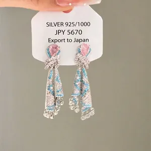Dettaglio degli orecchini rosa a goccia con nappe in cristallo blu su etichetta bianca