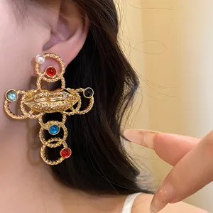 Detailed view of a retro gold-toned cross earring with colorful stones and lip motif