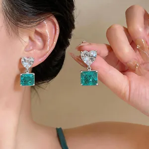 Detail view of silver stud earrings with heart-shaped zircon and green square pendant